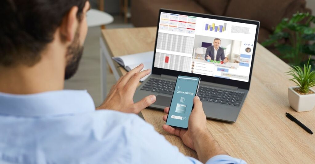 A man doing online banking on his phone and laptop. Is open banking safe?