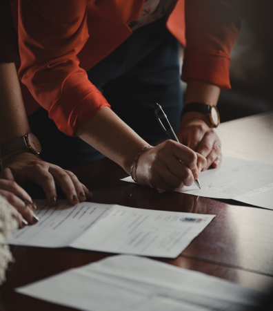 People signing contracts on a wooden desk.