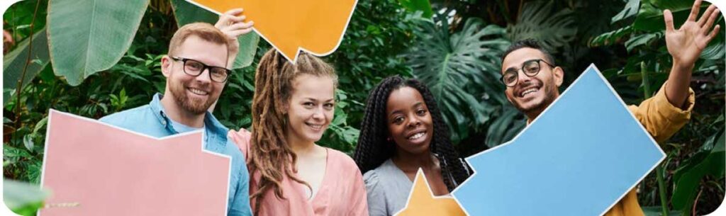 Four people smile in front of some plants.