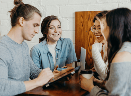 Four people laughing as they work at a desk.