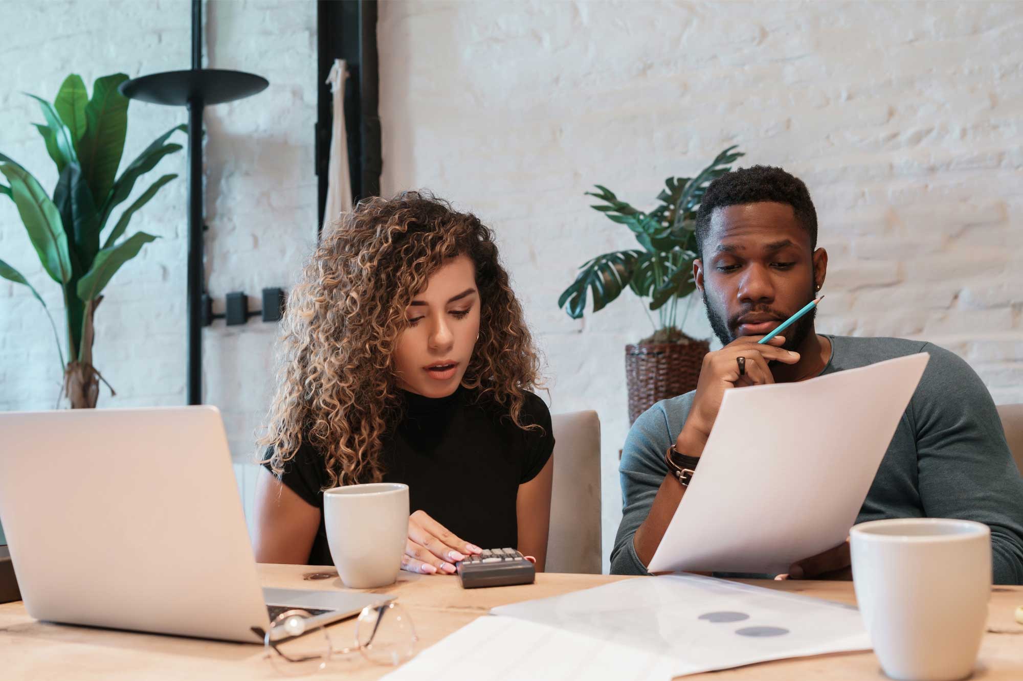 A woman works on a calculator while a man inspects some documents.
