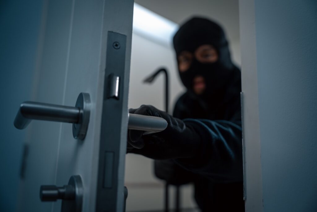 A burglar wearing a balaclava opens an unlocked door.