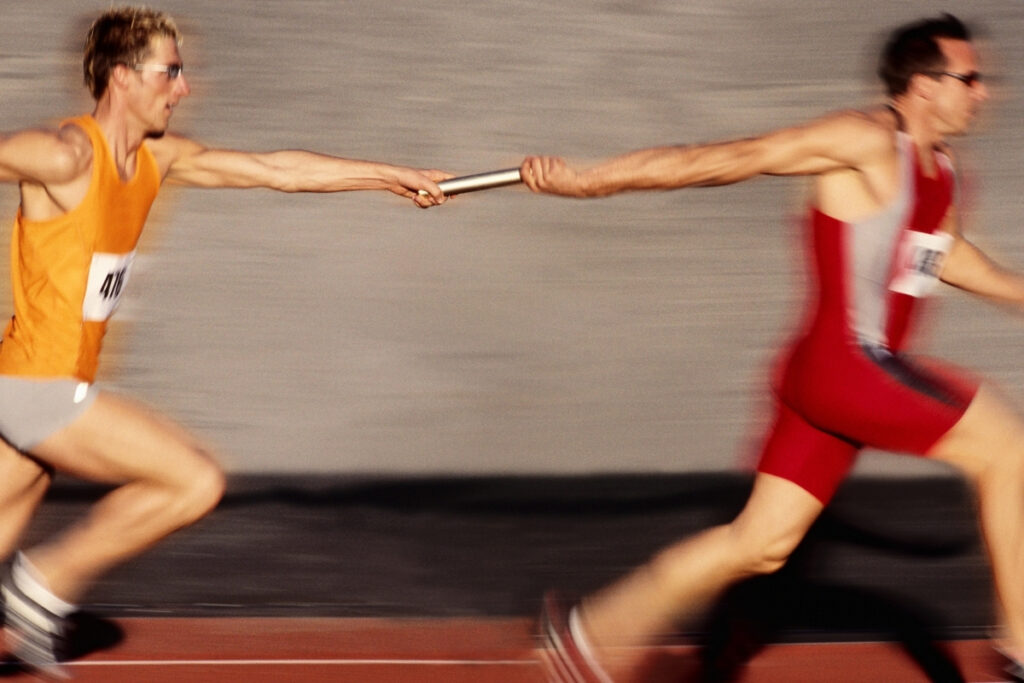 A relay race. One man hands the baton to another.